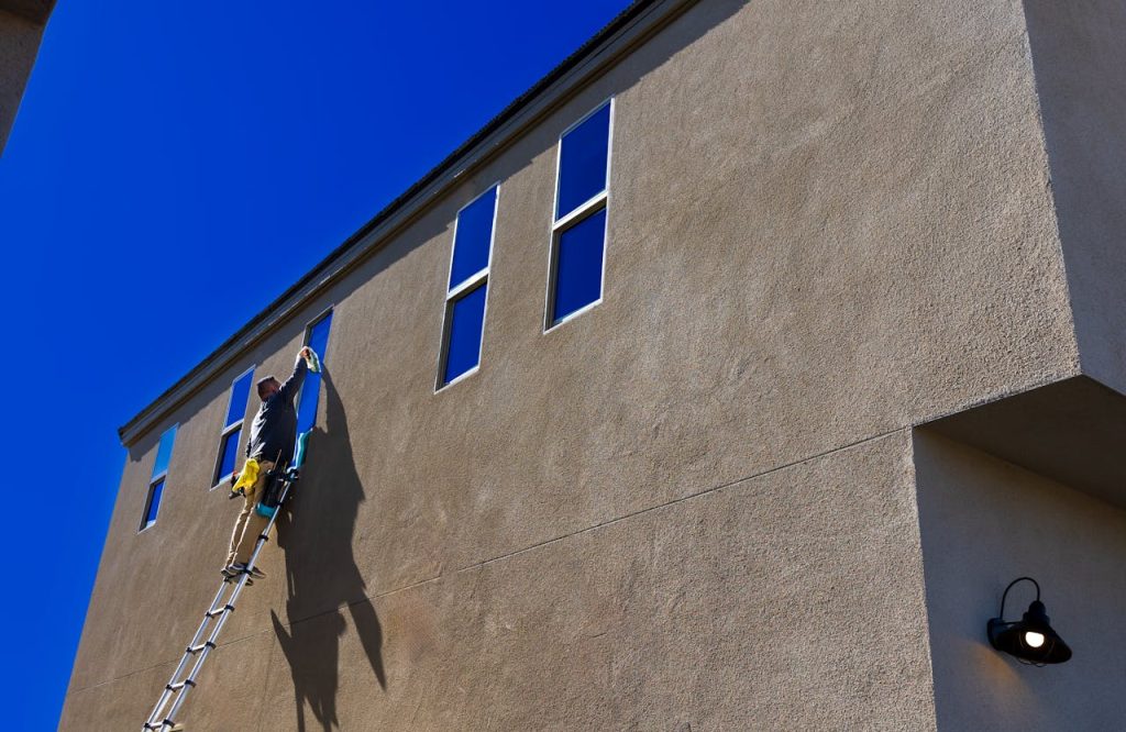 Crafting Captivating Headlines: Your awesome post title goes here Man using a ladder to clean exterior windows of a tall building under a clear blue sky.
